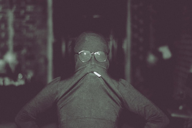 person wearing turtleneck over face with cigarette and glasses